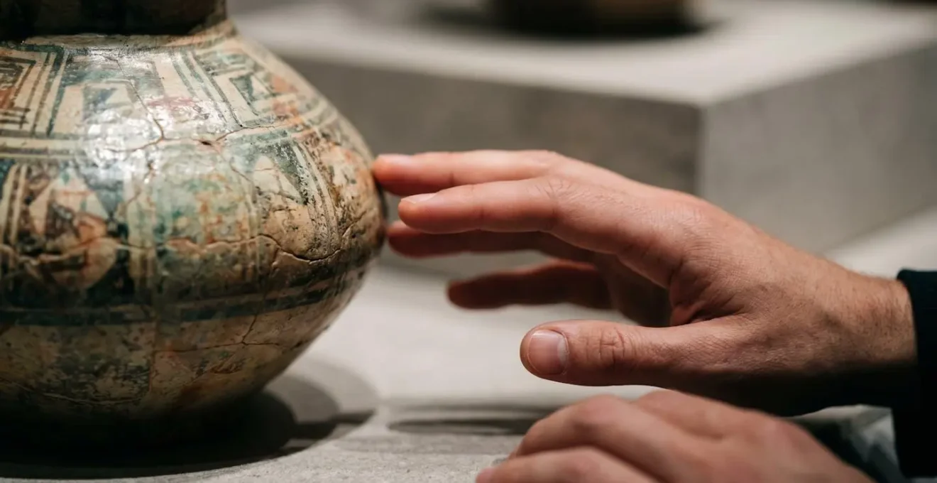 Extreme close-up of hands near ancient museum artifact showing embodied interaction